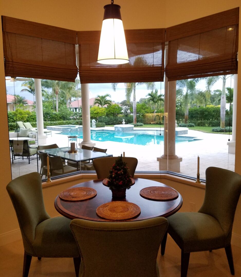 A dining room table with four chairs and a pool in the background.