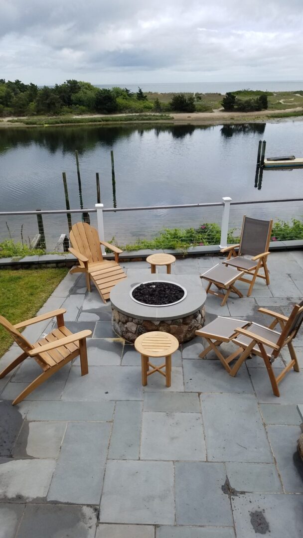 A patio with chairs and tables around an outdoor fire pit.